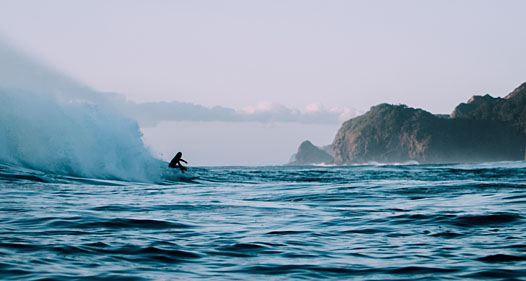 Person surfing on the water with landforms in the background.