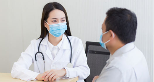 Asian female doctor speaks with a patient, both wearing protective masks.