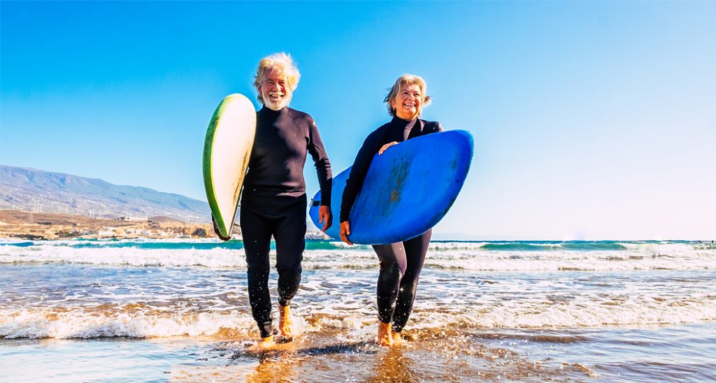Senior couple carry surfboards walking out of the ocean.