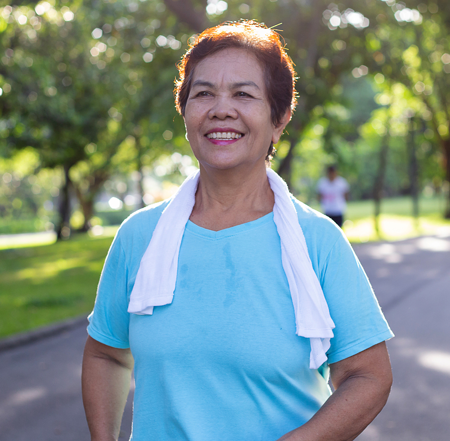 Senior Asian woman walks through a park with a smile.