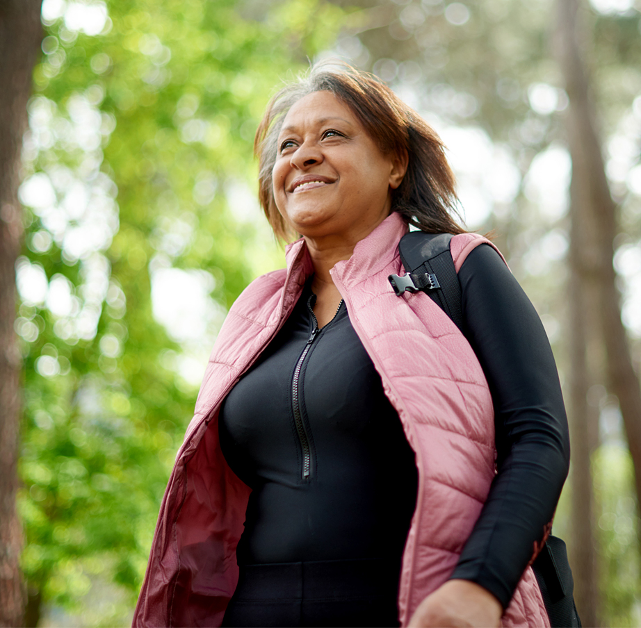 Mature African American woman in pink vest walks through a wooded area.