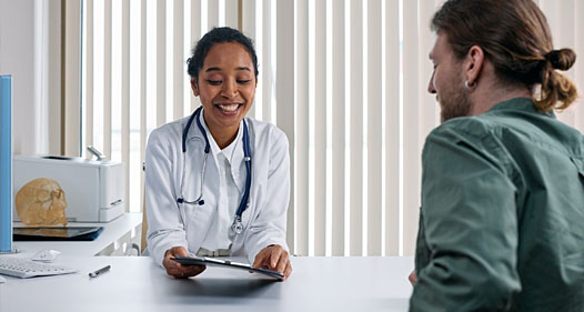 Female doctor smiles and looks at clipboard while talking to a patient.